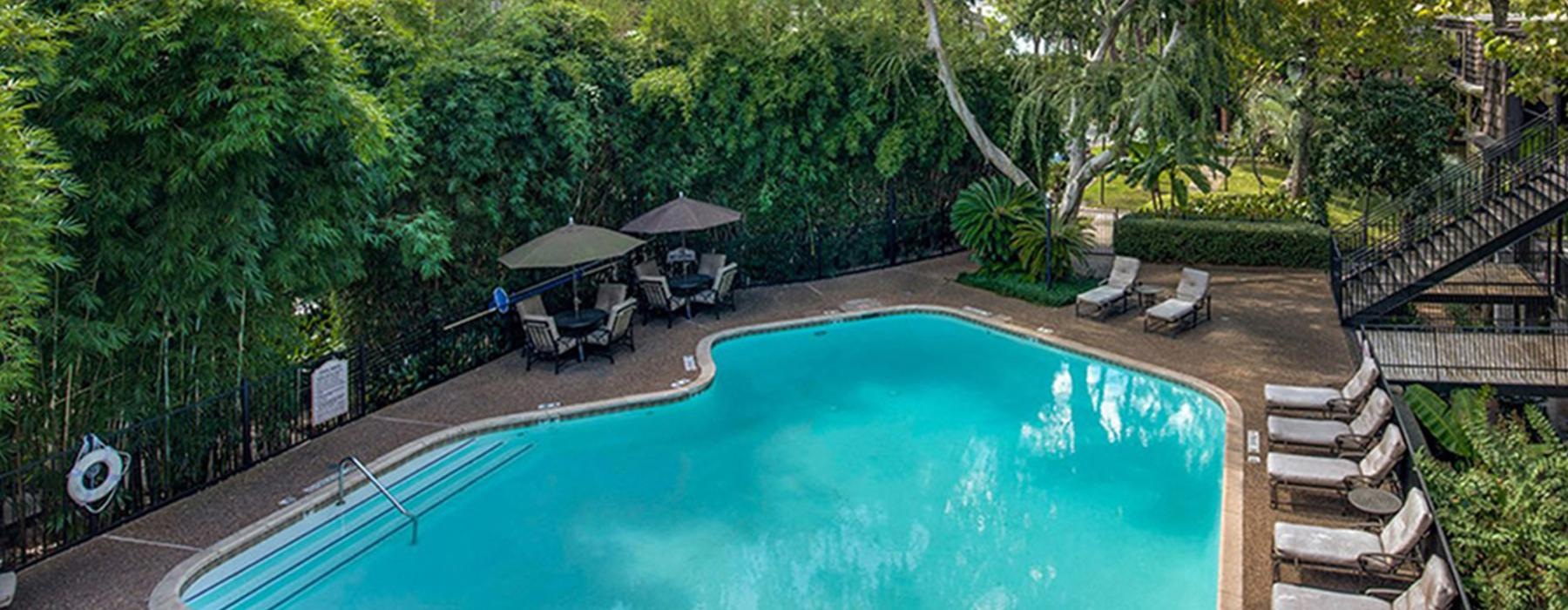 a pool with a deck and chairs by it and trees around it